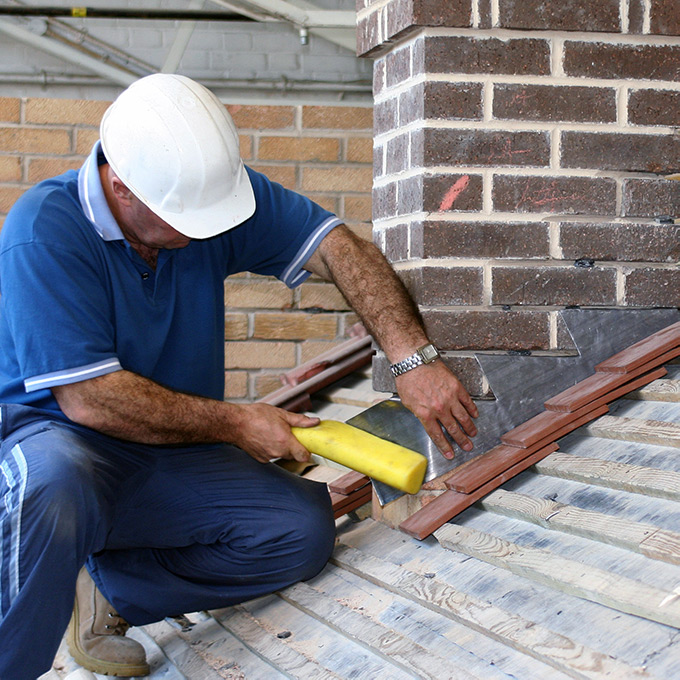 Roofer installing lead attachment between chimney and roof